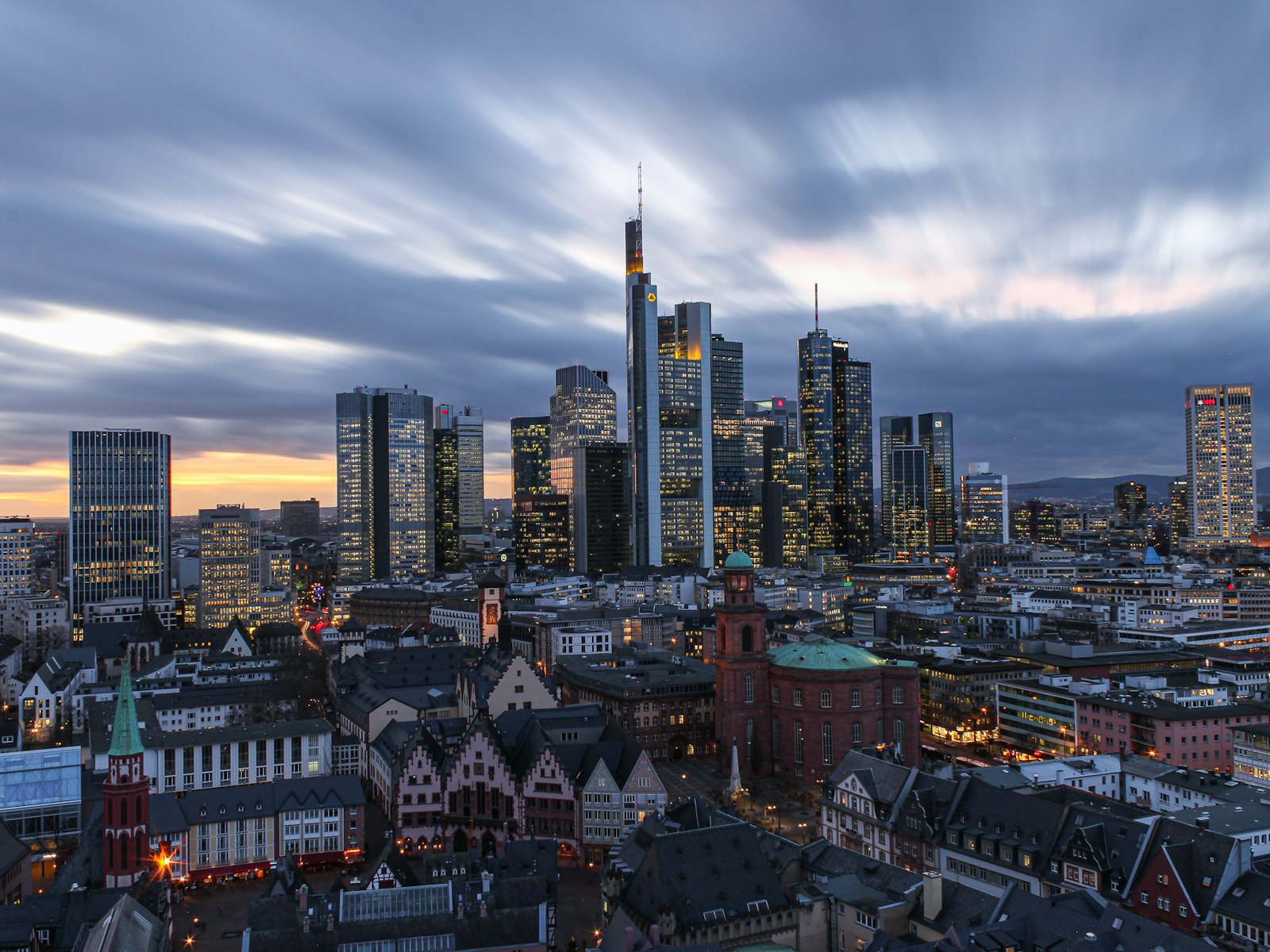 The Frankfurt financial-district skyline at dusk, its banking towers lit against a grey sky
